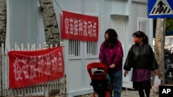 资料照:带着口罩推着婴儿车的女子走过北京的一处疫苗接种流动点。(2022年10月26日)