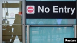 FILE PHOTO: International travelers (reflected in a closed door) arrive on the day that U.S. President Donald Trump's limited travel ban, approved by the U.S. Supreme Court, goes into effect, at Logan Airport in Boston, Massachusetts, U.S., June 29, 2017.