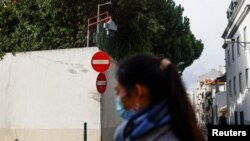 资料照片:一位女士从中国驻葡萄牙首都里斯本大使馆外走过,使馆墙头伸出一个监控摄像头,对着使馆外的街区。(2022年12月21日)