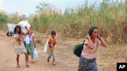Para warga Myanmar yang kehilangan tempat tinggal akibat situasi yang tak menentu di negaranya, berjalan membawa bantuan makan siang yang mereka dapat ke tenda tempat mereka tinggal di tepian sungai Moei di Mae Sot, Thailand, pada 5 Februari 2022. (Foto: AP)