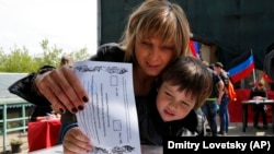 资料照:2014年5月,乌克兰东部的顿巴斯举行过一次公投。图为一名乌克兰妇女带着儿子5月11日在俄罗斯首都莫斯科参加公投投票。
