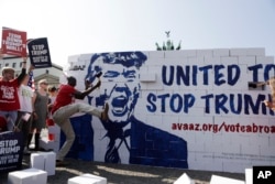 在德国柏林,反川普示威者捣毁所谓的“川普仇恨墙”,标语说,团结起来,阻止川普,选民在此登记