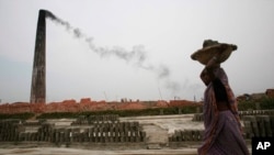 Asap mengepul dari cerobong asap saat seorang pekerja perempuan Bangladesh membawa tanah liat di ladang batu bata di Amin Bazar, pinggiran Dhaka, Bangladesh, Kamis, 14 Mei 2009. (AP/ Pavel Rahman)