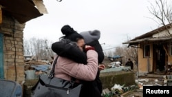 在基辅,一名当地居民在被俄罗斯导弹袭击破坏的房屋与朋友拥抱。(2022年12月29日)