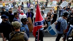 维吉尼亚夏洛特维尔市一名白人至上主义者手持南方邦联旗从反示威人群中走过。(2017年8月12日)