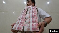 中国山西太原一家银行职员手捧成捆的人民币百元现钞。(资料照片)