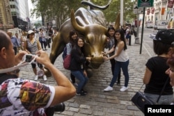 资料照:中国游客在纽约华尔街的铜牛前合影。(2015年8月24日)