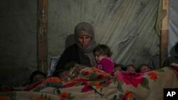 资料照片:在加沙地带汗尤尼斯的一处营地,瑞达·阿布·扎拉达(Reda Abu Zarada)用毯子盖住自己和孩子,准备在帐篷中入睡。(2024年12月19日)