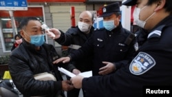 中国武汉一个街口设立的检疫站社区工作人员给一名男子测量体温,同时警察检查男子的证件。(2020年2月20日)