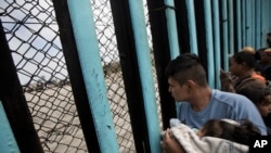 一个中美洲移民车队的人抱着孩子向边界墙对面张望(2018年4月29日)