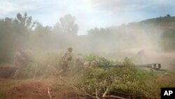 乌军士兵在乌东顿涅茨克地区为美国提供的M777榴弹炮盖上迷彩伪装。(2022年6月18日)