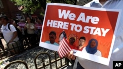 资料—在美国波士顿爱尔兰大饥荒纪念园举行的“在此停留”集会上,一名抗议者手持标语牌(2017年7月6日)