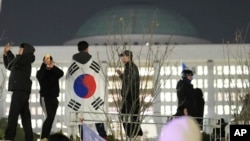 韩国首尔,一名身披韩国国旗的男子和其他几位民众站在国会大厦的墙上。(2024年12月4日)