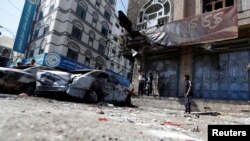 也门民众驻足观看萨那街头被毁掉的胡赛反叛武装与忠于前总统萨利赫的武装相撞的车辆。(2017年12月5日)