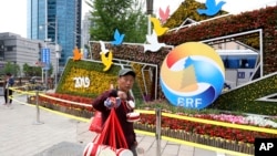 一名小贩路过宣传4月25日至27日在北京举行的“一带一路国际合作高峰论坛”的巨型花卉(2019年4月19日)