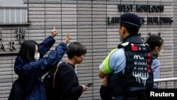 资料照:一名女子在香港西九龙裁判法院外等待根据国家安全法受到指控的47名民主活动人士的判决时打出支持的手势。(2024年5月30日)