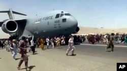 美国空军C-7运输机在喀布尔国际机场起飞时上百人在跑道上跟随奔跑。（2021年8月16日）
