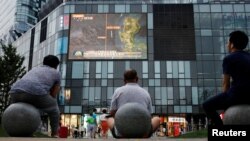 北京居民坐在一家商场外观看电视新闻节目。(2016年7月16日)