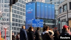 2025年1月21日, 上海街道上等候交通信号灯的行人与街头电子广告牌上显示的沪深股票指数。