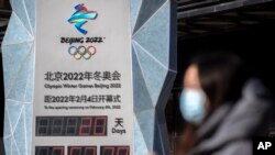 2022年1月15日,2022年北京冬季奥运会开幕前,一名戴着口罩的妇女走过倒计时钟(美联社)。