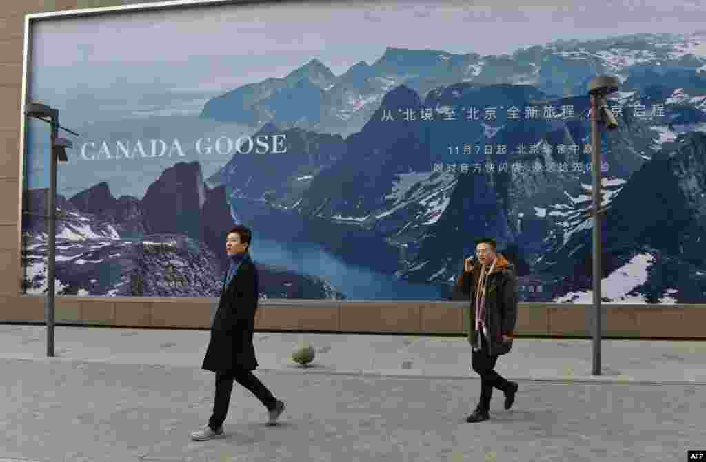 2018年12月15日,两名男子走过北京的“加拿大鹅”新店附近的广告牌。华为财务官孟晚舟12月在加拿大被捕后,中国逮捕了两名加拿大公民,中加关系紧张。加拿大鹅在北京首家商店的开张时间推迟了两周,但加拿大鹅表示推迟原因是建筑还在施工,而不是两国外交关系。有人在中国的社交媒体上鼓励民众抵制加拿大鹅,加拿大鹅在多伦多的交易市场价格一度下降了37%。全球奢侈品的购买人群中有超过三分之一来自中国。  