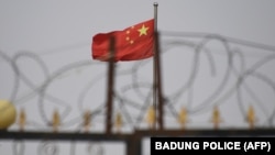 资料照片:中国国旗在新疆喀什南部地区一处建筑物的围栏铁丝网后飘扬。(2019年6月4日)