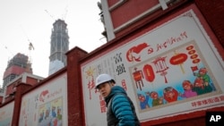 建筑工人走过北京一个居民小区外面,墙上有宣传牌《社会主义核心价值观:富强》《社会主义核心价值观:民主》(资料照片)