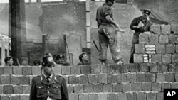 1961年10月7日,一名西柏林卫兵站在分隔东西柏林的混凝土墙前,同时,东德工人在为这道墙添砖加高。(资料照片)