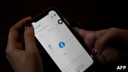 一名妇女使用手机在仰光查看Facebook,缅甸将军在夺权数天后下令互联网提供商限制访问Facebook。(2021年2月4日) (STR /法新社)