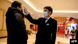 在上海的一个购物中心,一名保安在为顾客测体温。