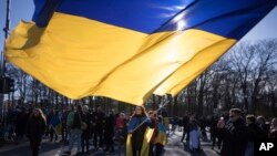Seorang perempuan mengibarkan bendera Ukraina raksasa dalam protes memperingati dua tahun invasi besar-besaran Rusia, di Gerbang Brandenburg, Berlin, Sabtu, 24 Februari 2024. (Foto: AP)