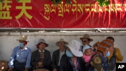 资料照片:在西藏拉萨一处寺庙附近,藏民在用汉语和藏语写成的政府宣传横幅下休息。(2021年6月3日)