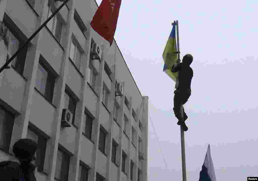 A man climbs a post to remove a Ukrainian flag as protesters hold a rally outside the mayor's office in Mariupol, April 13, 2014. 