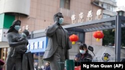 资料照片:中国武汉市,一名女子正走过带着口罩的雕塑面前。期间,世卫组织新冠溯源专家小组正在武汉考察。(2021年1月29日)