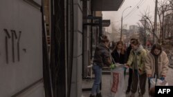 Місцева молодь прибирає розбите скло на місці ракетного обстрілу в Києві 20 грудня 2024 року. Roman PILIPEY/AFP