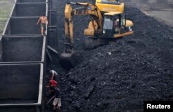 Seorang buruh (kiri) berjalan di tepi gerbong kereta kargo saat rekan-rekannya menyekop batu bara di tempat pembuangan batu bara. (Foto: Reuters)