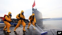 中国海军发布的照片显示,在青岛潜艇基地,穿着防护服的水兵清洁核潜艇