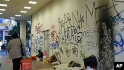 1月24号,希腊一名妇女从雅典一个地铁站外的流浪者身边走过。