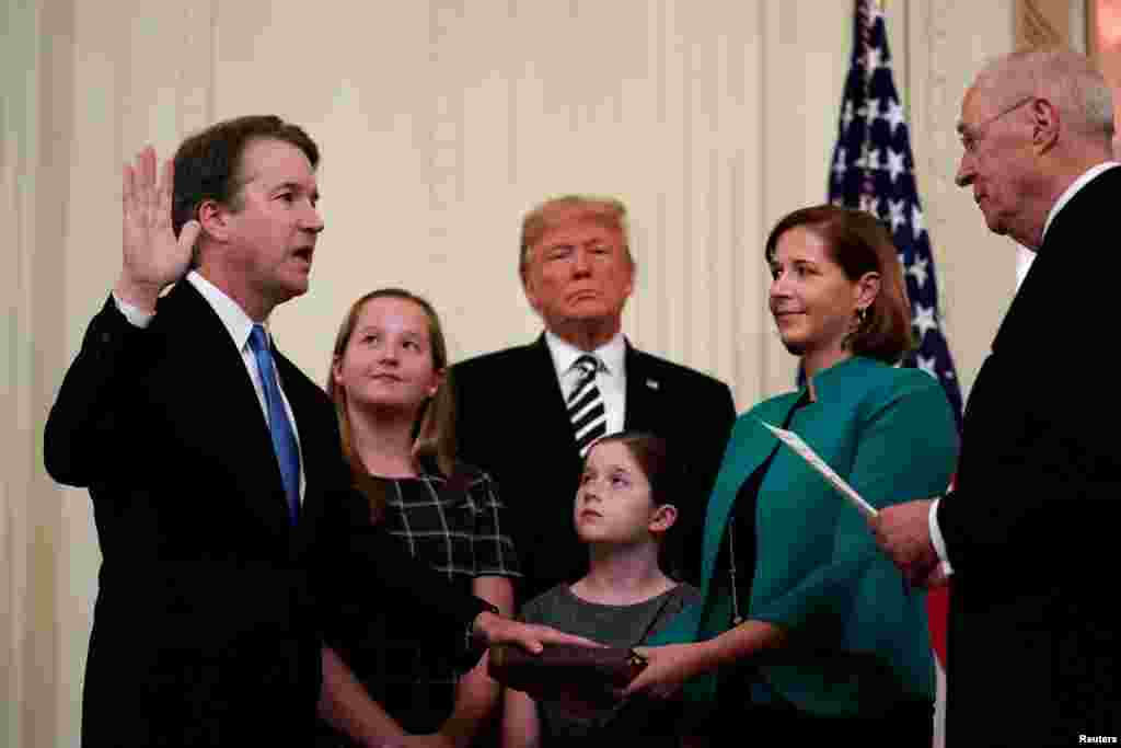 美国最高法院退休大法官肯尼迪在白宫带领新任大法官布雷特· 卡瓦诺宣誓就任。卡瓦诺夫人阿什利·卡瓦诺捧着圣经,美国总统特朗普和卡瓦诺的女儿在场(2018年10月8日)。特朗普和共和党人希望对这位53岁的保守派法官的任命,能够激发共和党选民在11月的中期选举中踊跃投票。中期选举将决定对国会的政治控制权。