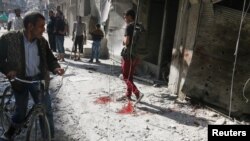 People inspect the damage as a civilian walks near blood stains at a market hit by air strikes in Aleppo's rebel-held al-Fardous district, Syria, Oct. 12, 2016.