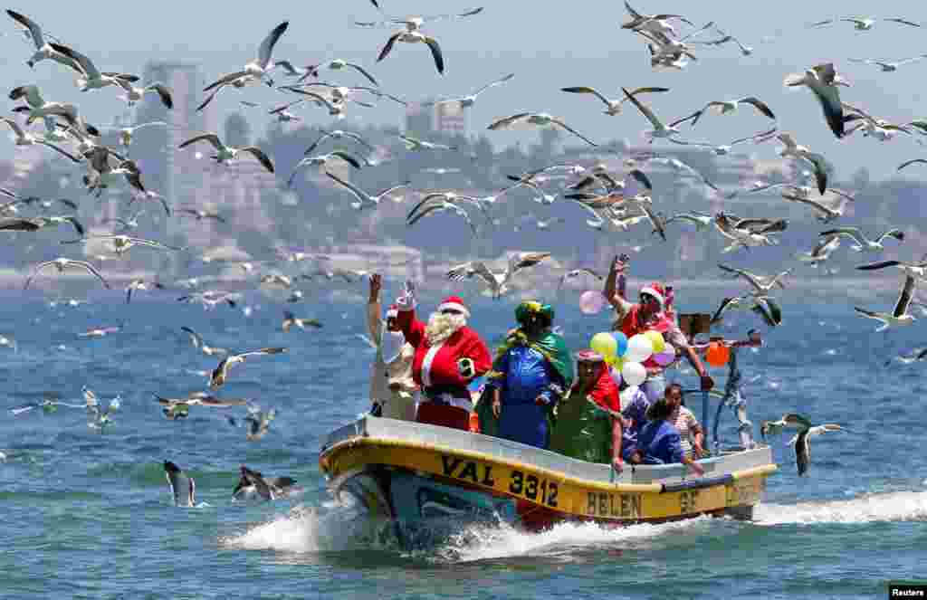 2017年12月24日,圣诞节前夕,智利瓦尔帕莱索海岸附近,一位穿着圣诞老人服装的男子在渔夫的船上挥手致意,群鸟飞翔。