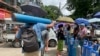 A man carries an oxygen tank while others line up with their oxygen tanks outside an oxygen refill station in Pazundaung township in Yangon, Myanmar, Sunday, July 11, 2021. Myanmar is facing a rapid rise in COVID-19 patients and a shortage of oxygen supplies just as the country i