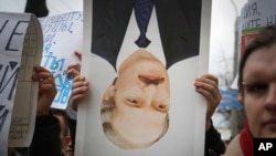 在白俄罗斯明斯克的集会上,一名抗议者手持翻过来的卢卡申科肖像表达不满。(美联社:2017年3月15日)