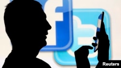 一名在脸书和推特的徽标前玩手机男子的侧影。(资料照片)