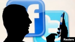 一名在脸书和推特的徽标前玩手机男子的侧影。(资料照片)
