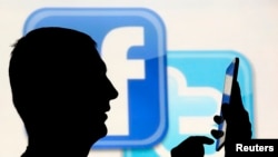 一名在脸书和推特的徽标前玩手机男子的侧影。(资料照片)