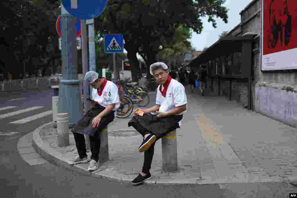 2018年8月22日,北京,两名餐馆工作人员坐在路边的石墩上。他们身后是关于马克思和恩格斯的宣传画。他们所在的餐馆如果是民营的而且雇佣职工至少8人,按照马克思的理论,就是剥削。马克思这一论点在改革开放初期曾经阻碍了中国私营企业的发展,后来被突破了,一大原因是要解决就业问题。