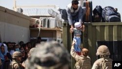 美国陆军发布的照片显示,在喀布尔哈米德·卡尔扎伊国际机场,一名阿富汗男子把他的孩子交给英军伞兵,美国陆军82空降师成员在旁执行安全警戒。(2021年8月26日)