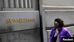 一名戴着口罩的女子走过纽约华尔街街牌。(2020年3月6日)