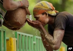 Seorang pekerja India beristirahat sejenak untuk minum air dari teko tanah di sore yang panas di Allahabad, India. (Foto: AP)